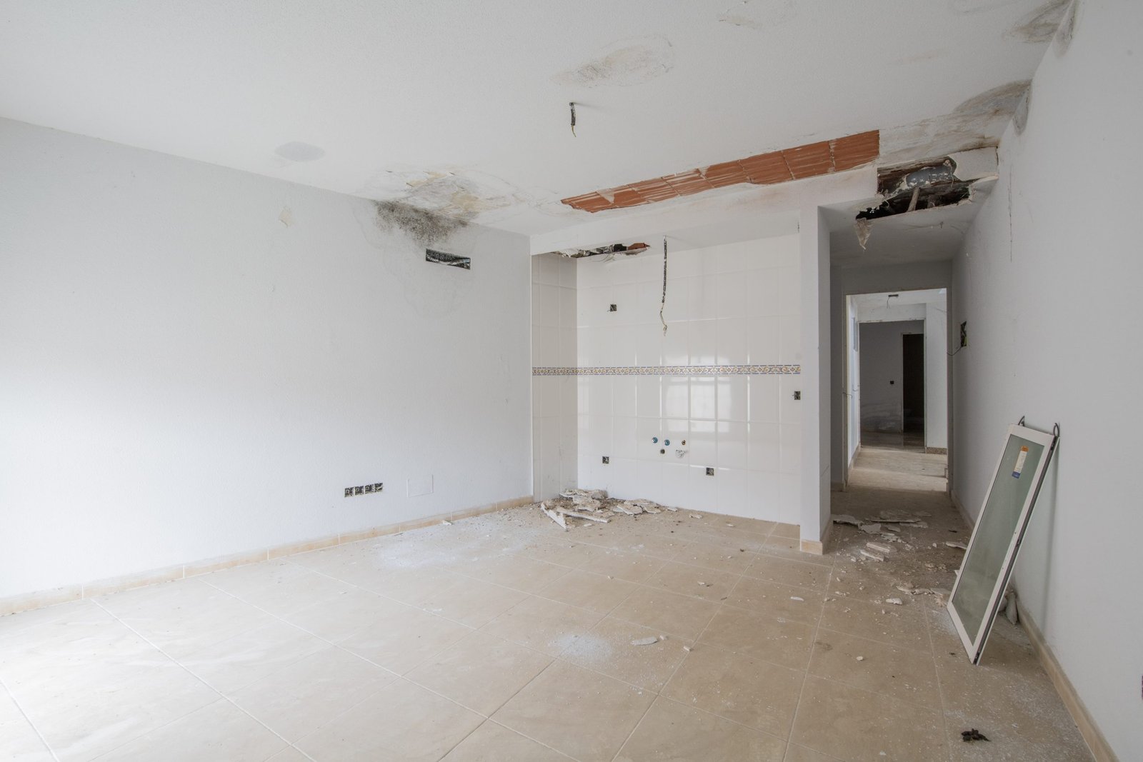 An unfinished empty room with kitchen tiles on one wall and heavy damage caused by water leaks An unfinished empty room with kitchen tiles on one wall and heavy damage caused by water leaks